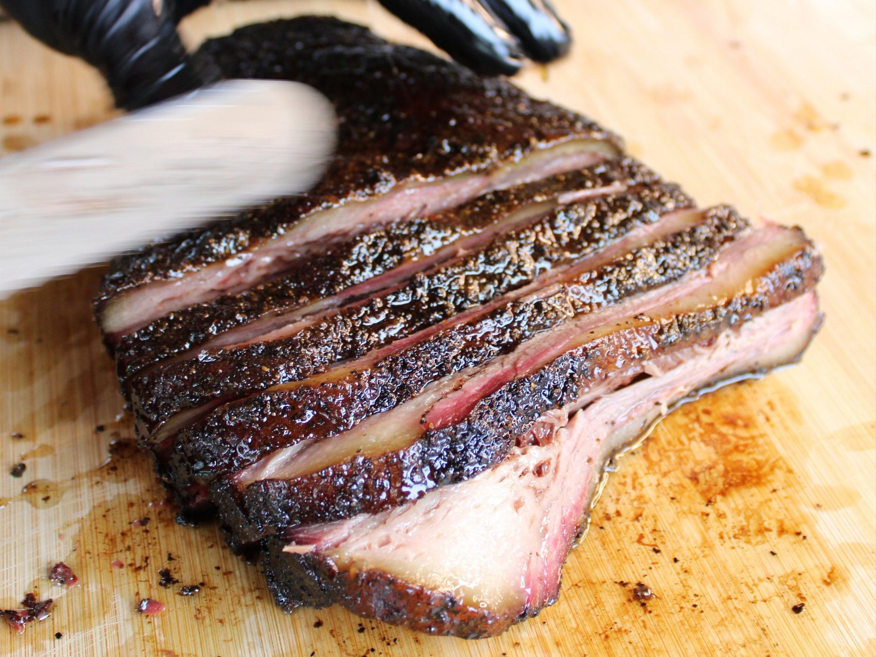 Slicing Texas-style brisket with a black-pepper bark and a visible smoke ring